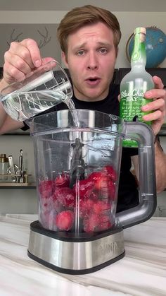 a man is pouring water into a blender filled with strawberries and raspberries