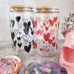 three glass jars with hearts painted on them next to a pink bowl and other items