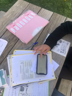 a person sitting at a picnic table with notebooks, papers and a cell phone