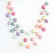 a multi - colored felt ball necklace is displayed on a white surface with beads hanging from it's sides