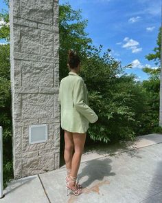 a woman standing on the sidewalk in front of a stone building with trees and bushes behind her