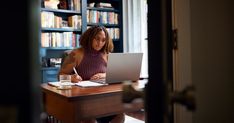 a woman sitting at a desk in front of a laptop computer with a pen and paper on it