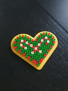 a heart shaped beaded object sitting on top of a wooden table next to a black surface