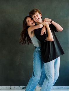 two people hugging each other while standing in front of a wall