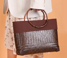 a woman is holding a brown and black handbag in her right hand while wearing a white shirt