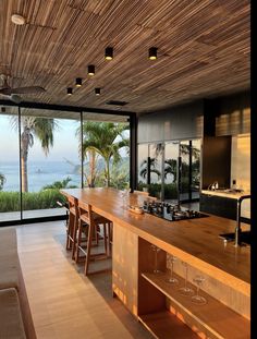 a large kitchen with an island counter top and wooden ceilinging, overlooking the ocean