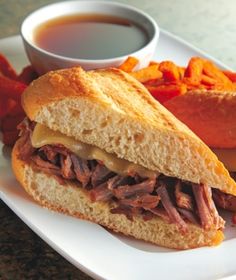 a roast beef sandwich and sweet potato fries on a white plate with dipping sauce in the background