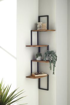 three wooden shelves with plants and books on them in the corner of a white room