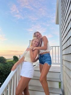 two beautiful young women standing next to each other on a porch with the sun setting behind them