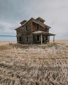 an old abandoned house sitting in the middle of a dry grass field on a cloudy day