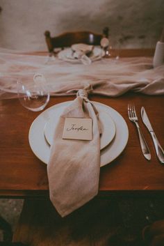 a place setting with napkins, silverware and wine glasses on a wooden table