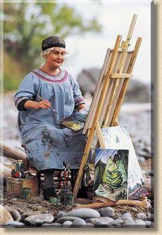 a statue of a woman sitting next to an easel with paintings on the ground