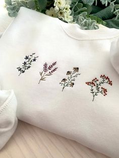 three embroidered t - shirts sitting on top of a wooden table next to some flowers