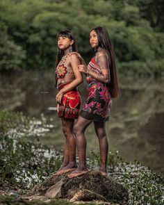 two people standing on top of a rock next to a river