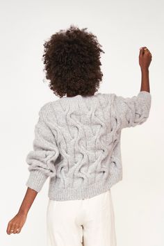 a woman in white pants and a gray cable knit sweater is pointing at something with her right hand