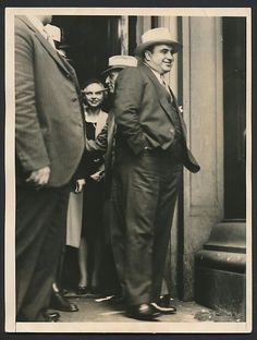 an old black and white photo of two men standing in front of a building with other people