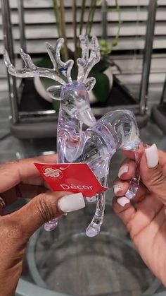 two hands are holding a glass reindeer ornament with a red tag on it