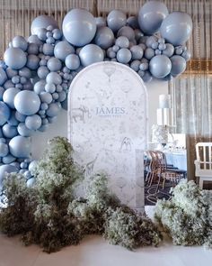 a table topped with lots of balloons next to a white and blue wall filled with trees