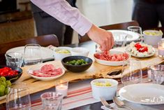 a person preparing food on a table with plates and glasses in front of them,