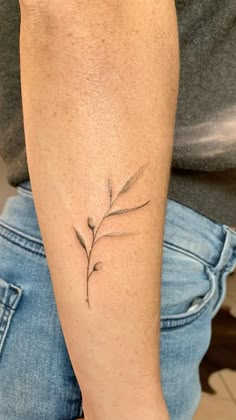 a woman's arm with a small branch tattoo on the left side of her arm