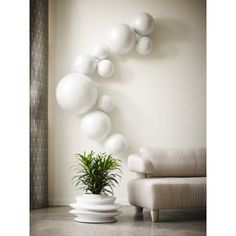 white balloons are hanging on the wall next to a chair and potted plant in a living room