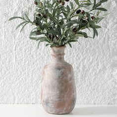 a vase with some plants in it sitting on a table next to a white wall