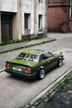 a green car parked on the side of a road next to an old brick building