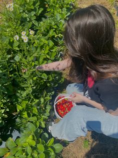 a woman sitting on the ground picking strawberries from a bush with her hands outstretched