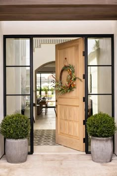 an open door with a wreath on it and two potted plants in the foreground