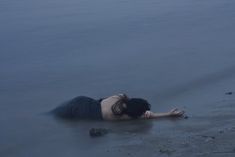 a woman is laying on the beach with her head in the water and arms out