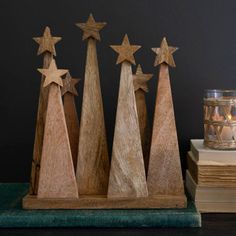 three wooden christmas trees on a table next to some books and a candle in a glass