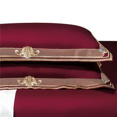 two pillows with gold trim on them sitting next to each other