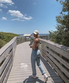 a woman walking down a wooden walkway next to the ocean with her hand in her pocket