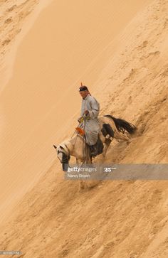 a man riding on the back of a brown horse in the sand covered desert area