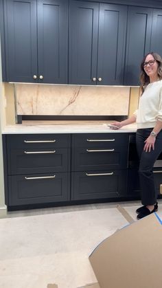 a woman standing in front of a kitchen counter top with drawers and cabinets behind her