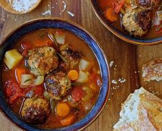 two bowls filled with meatballs and vegetables on top of a wooden table next to bread