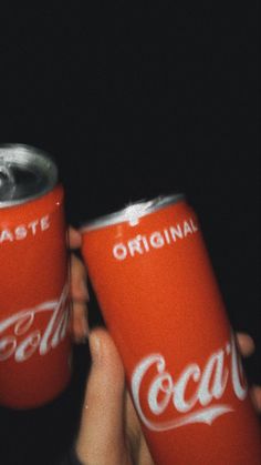 two coca - cola cans are being held up by someone's hands with their fingers