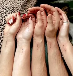 four people with matching tattoos on their arms holding each other's hands in the air