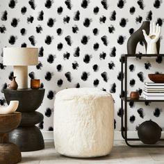 a living room with black and white wallpaper, a round footstool and two lamps