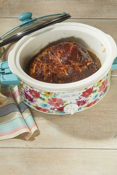 a slow cooker filled with food on top of a wooden table next to utensils