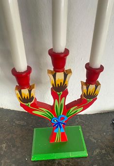 three candles are sitting on top of a green stand with red and yellow flowers painted on it