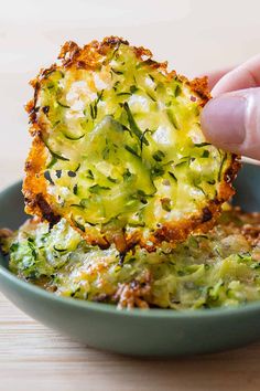 someone is dipping broccoli into some kind of food in a blue bowl on a wooden table