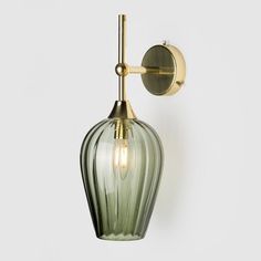 a green glass wall light with a brass finish and an arm that is attached to the wall