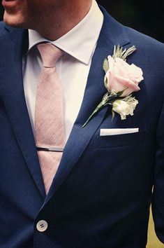 a man wearing a blue suit and pink tie with a white rose on his lapel