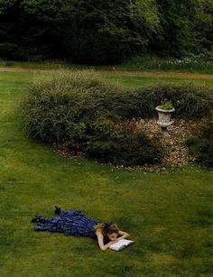 a woman laying on the grass reading a book