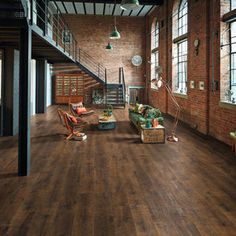 a living room with wooden floors and brick walls, along with large windows on the second floor