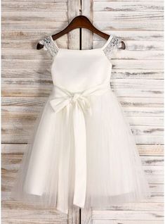 a white flower girl dress hanging on a wooden wall