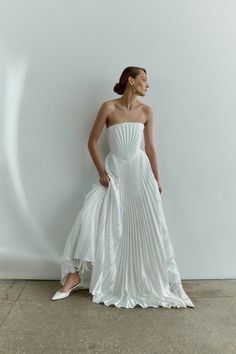 a woman in a white dress leaning against a wall