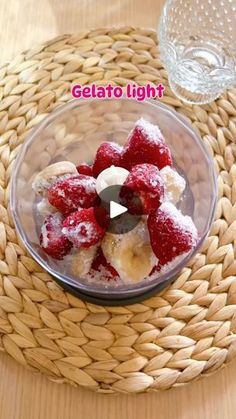 a bowl filled with bananas and strawberries on top of a woven place mat next to a glass vase