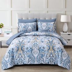 a bed with blue and gold comforters in a room next to a white wall